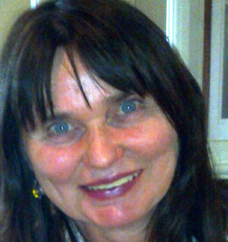 Claire Hawthorn, a woman with straight dark hair and blue eyes, smiles at the camera. She is indoors, with a beige wall and part of a doorframe visible in the background.