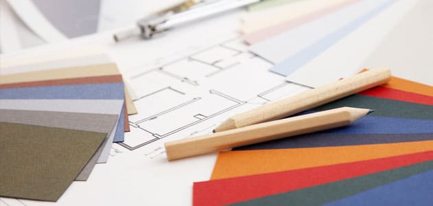 A set of colour swatches and two pencils are laid on top of an architectural floor plan, with a pen partially visible in the background—capturing Andre Paul Gaffney Interior Designer’s creative process.