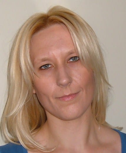 Margaret Janicka, a woman with straight blonde hair and light skin, is looking at the camera with a neutral expression, wearing a blue top against a plain background.