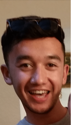A young man with short dark hair smiles at the camera. Phillip Lacy is wearing sunglasses on top of his head and appears to be indoors.