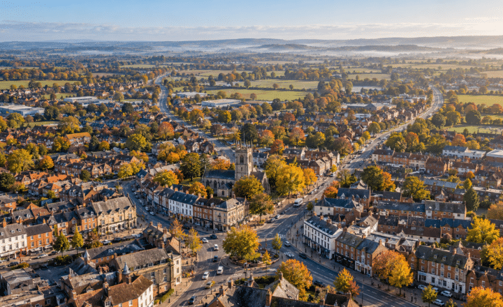 Aerial view of a small town with a central church, surrounded by autumn trees, houses, and roads—adult education centres supported by local funding blend into the landscape against distant hills and a clear blue sky.